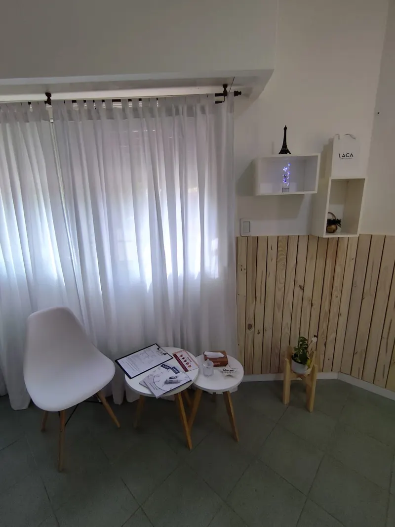 Rincón de espera con silla blanca, mesitas y revestimiento de madera